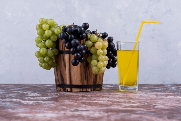 A bunch of green and red grapes in a bucket and a glass of juice