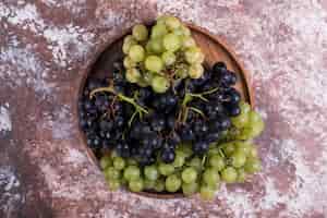 Foto gratuita un grappolo di uva verde e rossa in un piatto di legno