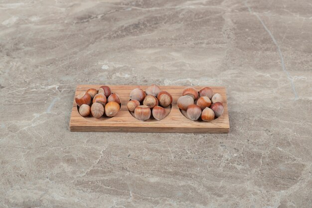 Bunch of hazelnuts in wooden plate on marble background. High quality photo