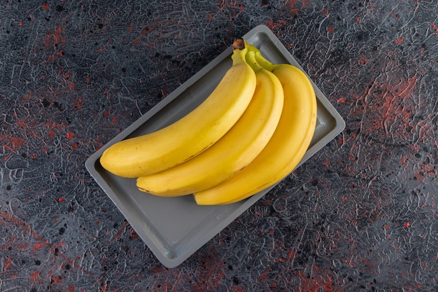 Bunch of juicy yellow banana placed on dark plate.