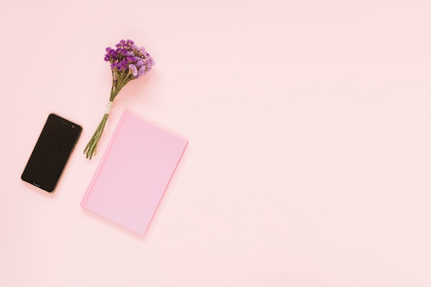 Free photo bunch of lavender flowers; cellphone and diary on pink backdrop