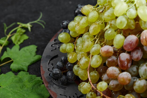 A bunch of mixed grapes on a ceramic plate with leaves. High quality photo