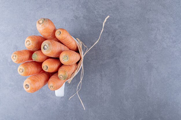 Бесплатное фото Букет из моркови в чашке на мраморной поверхности.