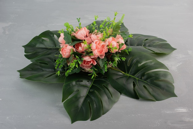 Bunch of pink roses with leaves on grey surface.