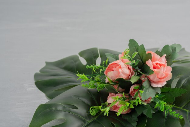 Букет из розовых роз с листьями на серой поверхности.