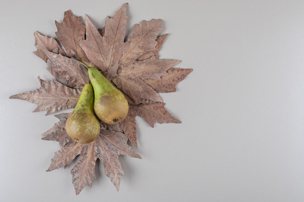 Foto gratuita mazzo di foglie di platano sotto due pere su marmo