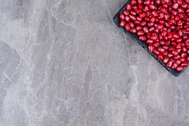 Bunch of pomegranate seeds on black plate. 