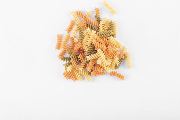 Bunch of raw colorful fusilli pasta on white surface.