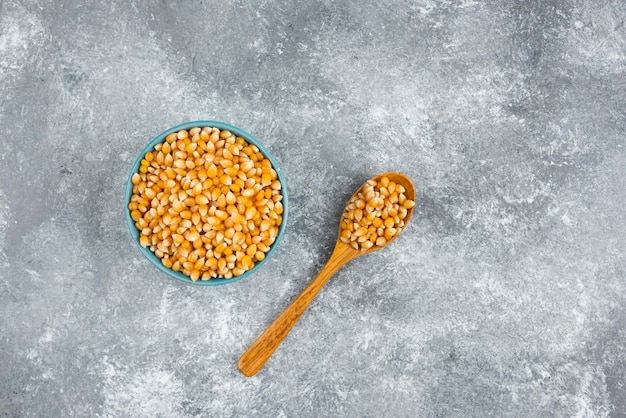 Bunch of raw corn seeds in blue bowls and wooden spoon.