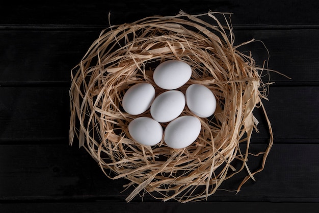 Букет из сырых свежих яиц в птичьем гнезде на черной поверхности. Фото высокого качества