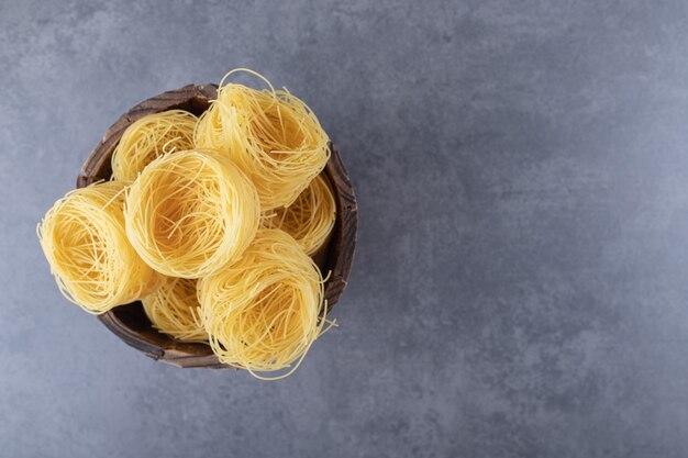 Bunch of raw pasta nests in wooden bucket.