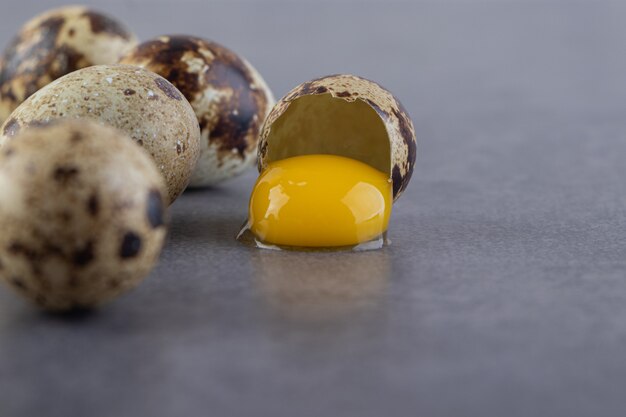 Bunch of raw quail eggs and egg yolk on stone table.