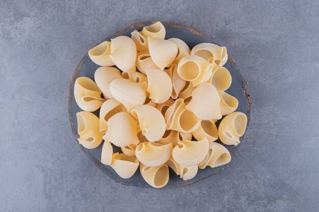 Bunch of raw shell pasta on wood piece.