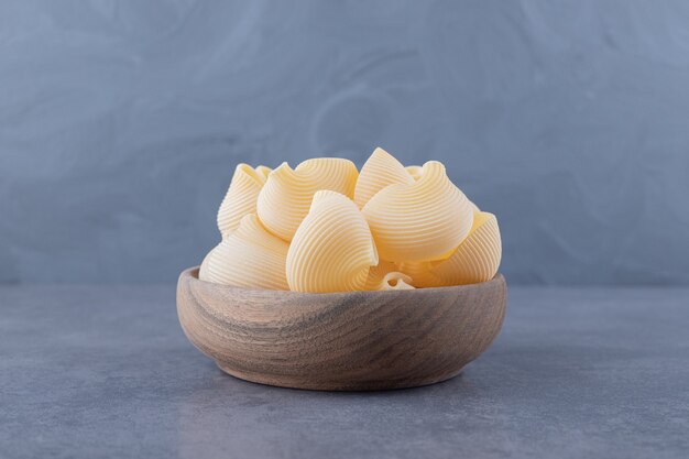 Bunch of raw shell pasta in wooden bowl.