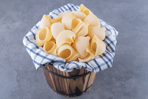 Bunch of raw shell pasta in wooden bucket.