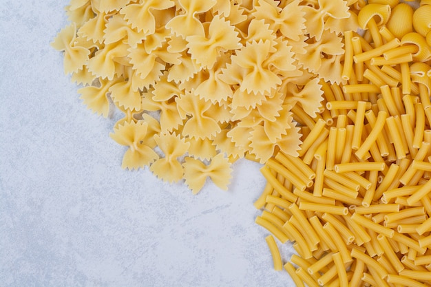 Bunch of raw spiral and farfalle pasta on stone surface