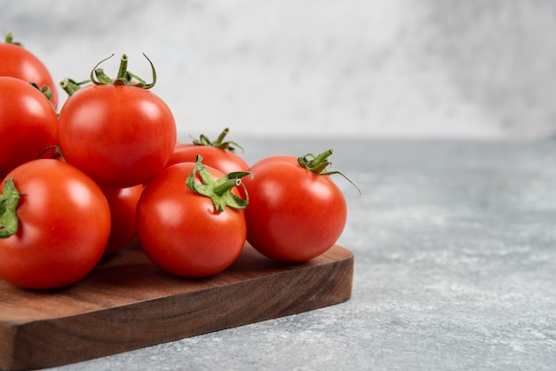 Bunch of red fresh tomatoes on wooden cutting board.