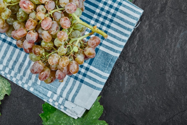 A bunch of red grapes with leaves and blue tablecloth on dark background. High quality photo