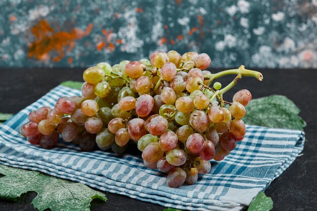 A bunch of red grapes with leaves and blue tablecloth on dark table. High quality photo