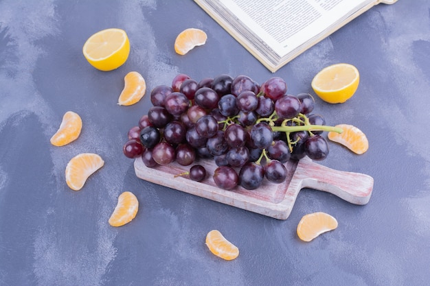 A bunch of red grapes on wooden platter with mandarines around.