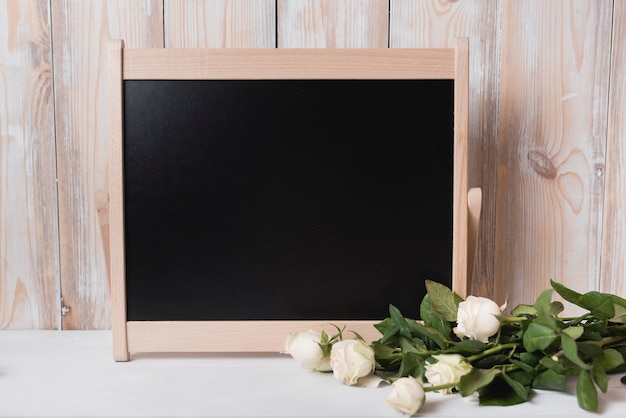 白い机の上に木製の小さな黒板とバラの束