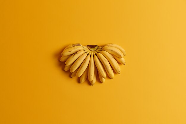 小さな熟したベビーバナナの束には、黄色の背景に分離された健康に不可欠な栄養素が含まれています。夏の果物のコンセプト。フラットレイ、上面図。天然ビタミン源。ダイエットと健康食品