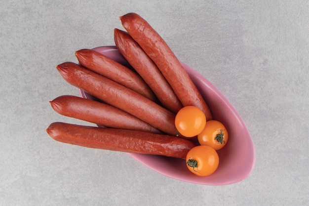 Bunch of smoked sausages and tomatoes in pink bowl.