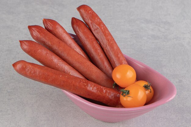 Bunch of smoked sausages and tomatoes in pink bowl.