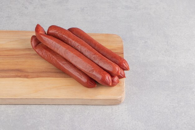 Bunch of smoked sausages on wooden board.