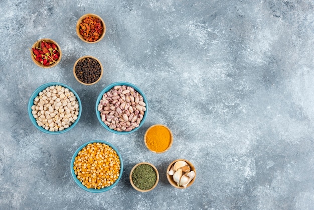 Bunch of spices and bowls of beans, corns on marble background.