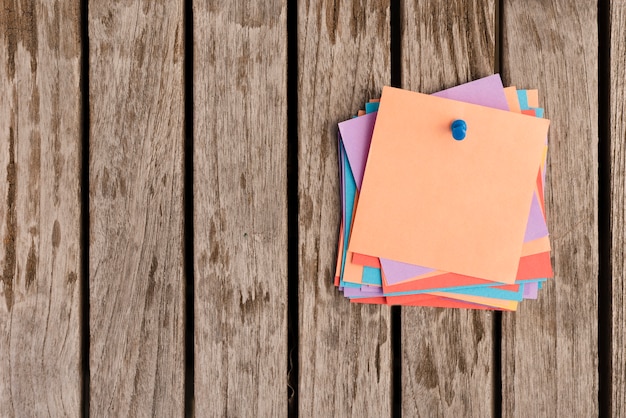 Bunch of sticky notes attached with blue push pin on wooden table