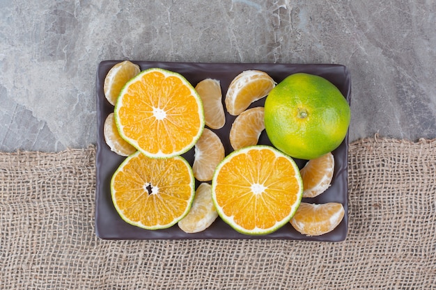 Bunch of tangerine and segments on black plate. 