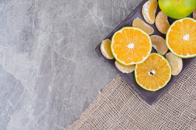 Bunch of tangerine and segments on black plate. 