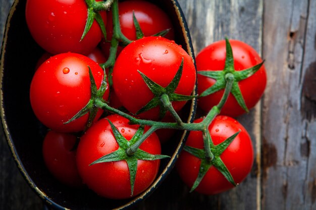 A bunch of tomatoes in a pot on a old wooden background. top view.