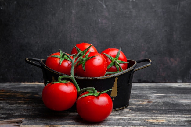 A bunch of tomatoes in a pot on a old wooden and black background. side view.