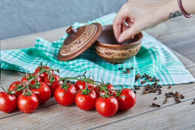 Bunch of tomatoes with branch and woman hand taking cloves from a bowl on wooden table