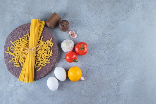 Bunch of uncooked spaghetti in rope with fresh red tomatoes and garlic.