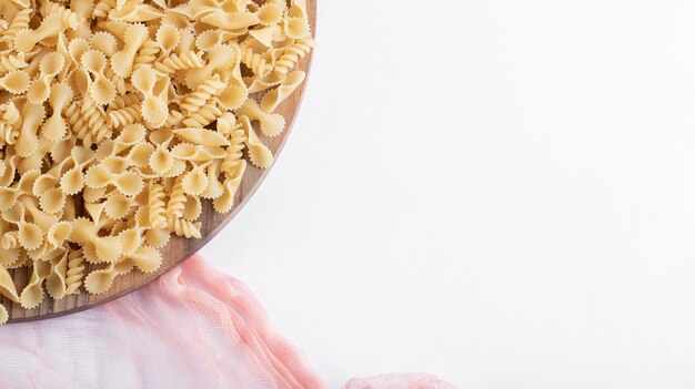 Bunch of various pasta on wooden plate with pink cloth.