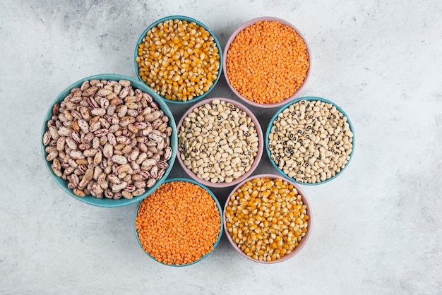 Bunch of various uncooked beans, corns and red lentils in bowls.