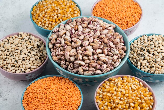 Bunch of various uncooked beans, corns and red lentils on marble surface.