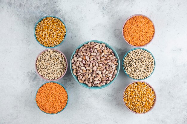 Foto gratuita mazzo di vari fagioli crudi, mais e lenticchie rosse sulla superficie di marmo.