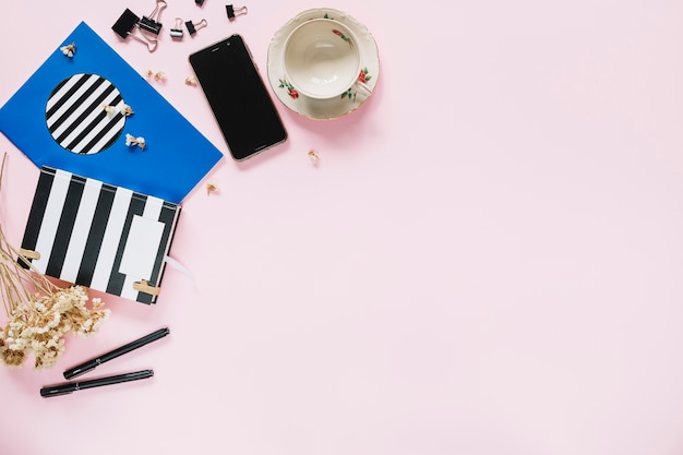 Bunch of white flowers with stationery; mobile phone and empty cup on pink backdrop