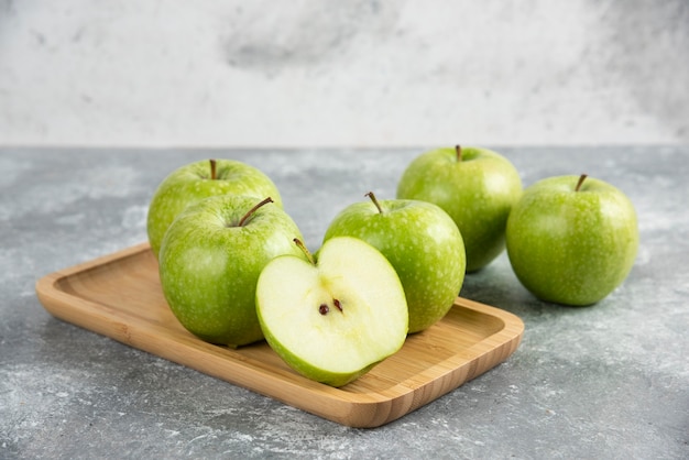 Bunch of whole and sliced green apples on wooden plate.