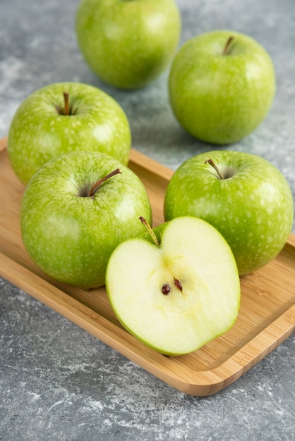Bunch of whole and sliced green apples on wooden plate. 