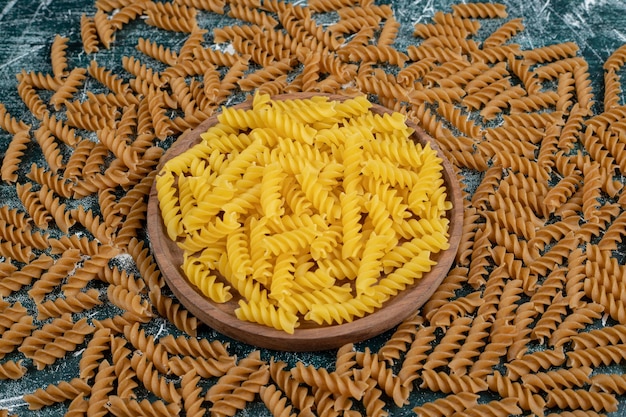 Mazzo di pasta fusilli gialla e marrone su spazio blu.