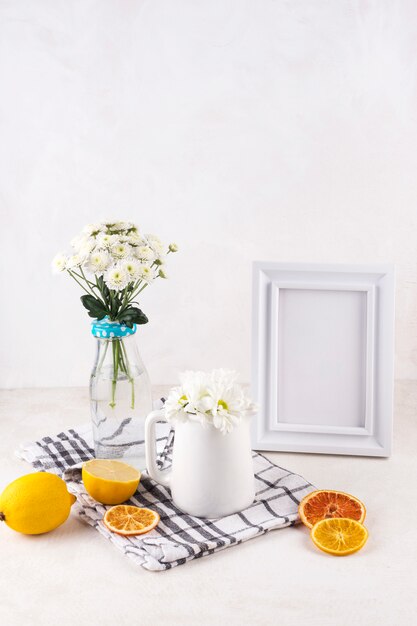 Bunches of fresh flowers in vase near fruits and photo frame