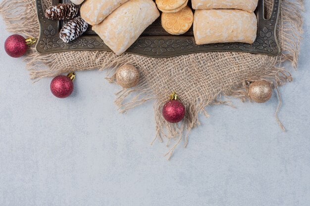 Bundle of assorted cookies on an ornate tray next to christmas baubles on marble surface