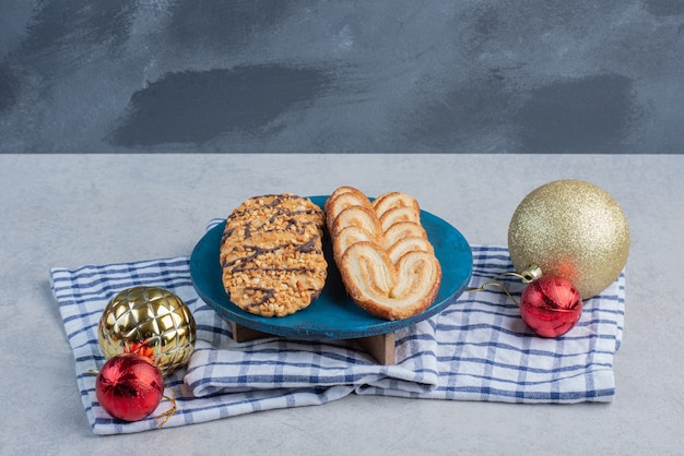 Foto gratuita pacchetto di biscotti su una tavola blu accanto alle bagattelle di natale su un asciugamano sulla superficie di marmo