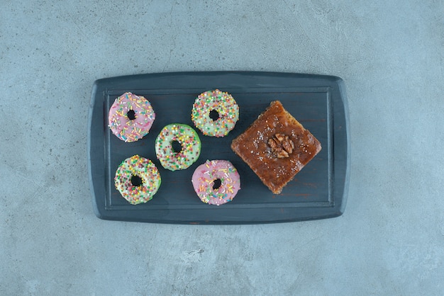 Free photo bundle of donuts and a piece of bakhlava on a navy board on marble surface