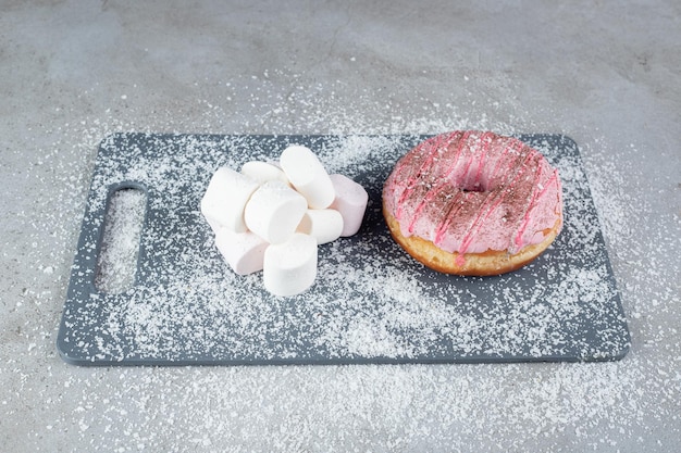 Bundle of marshmallows and a donut on a coconut power covered board on marble surface